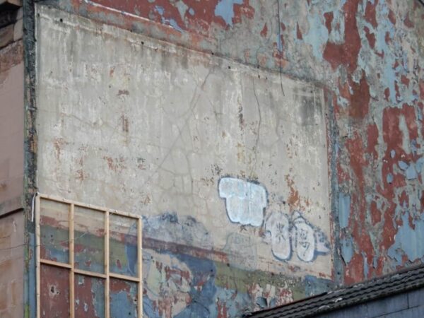 Graffiti and flaking paint on a wall that used to have a ghostsign for Ecko Radio