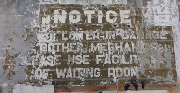 Painted sign in English on a Paris wall saying 'Do not loiter in garage, or bother mechanics. Please use facilities of waiting room'