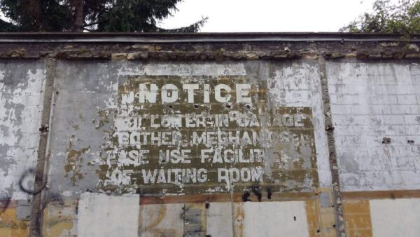 Painted sign in English on a Paris wall saying 'Do not loiter in garage, or bother mechanics. Please use facilities of waiting room'